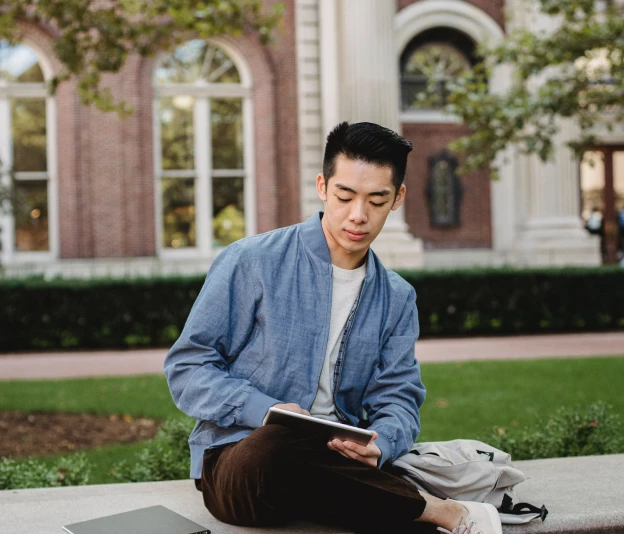 university-student-sitting-on-a-bench University student sitting on a bench and reading from tablet.