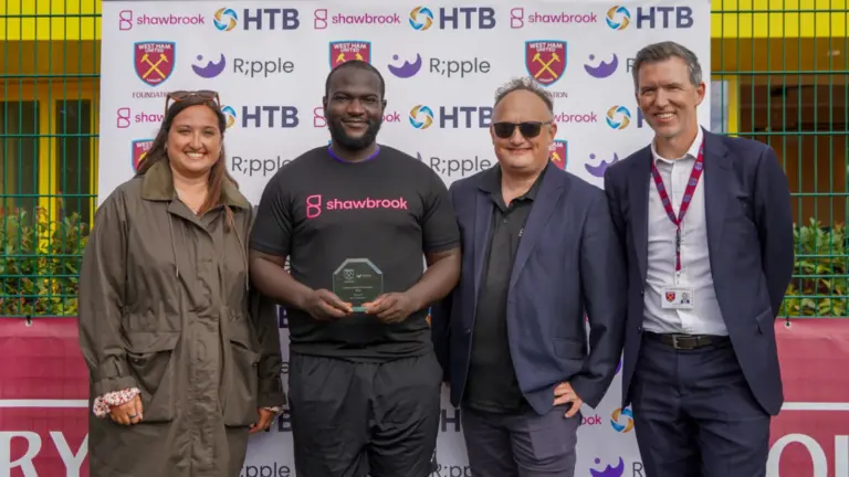 Four people at the Ripple and West Ham United Foundation tournament, one holding a glass award in a Shawbrook shirt.